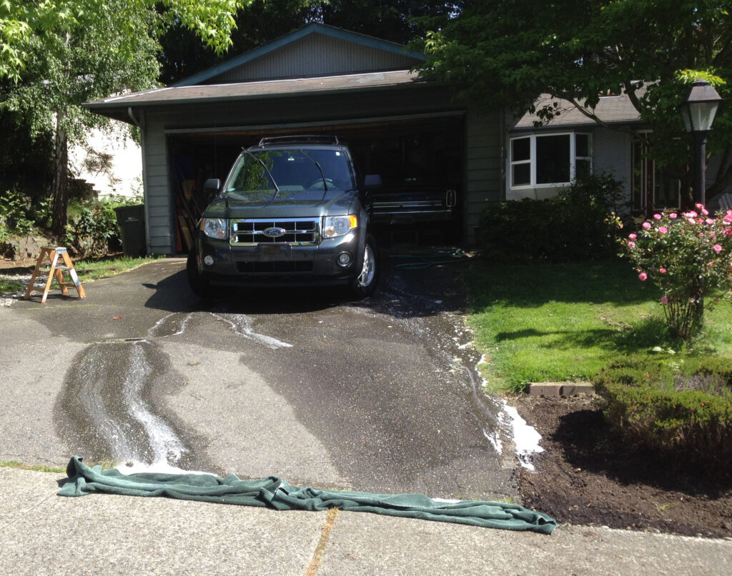 A car is being washed on a sloped driveway. Rolled up towels are placed at the bottom of the driveway to divert water into flower beds