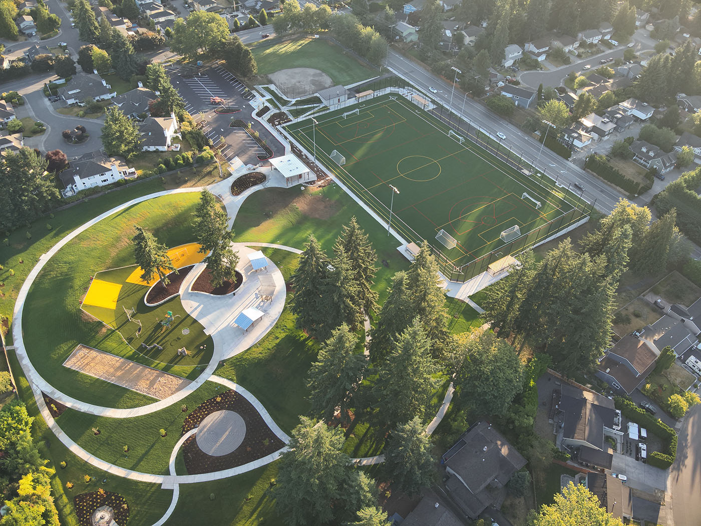 Aerial image of a park with a large ballfield, grassy hills, trees, and a children's playground.